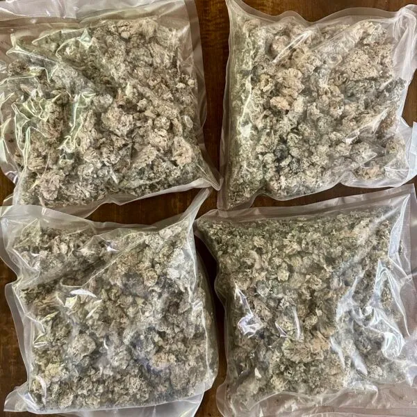 Four vacuum-sealed bags filled with cannabis flower on a wooden surface.