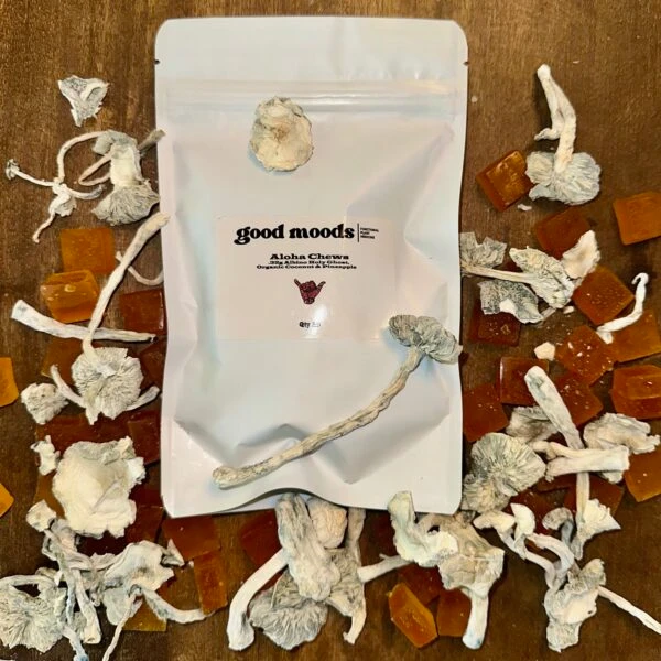 Good Moods Aloha Chews pouch surrounded by dried mushrooms and pineapple gummies on a wooden surface.